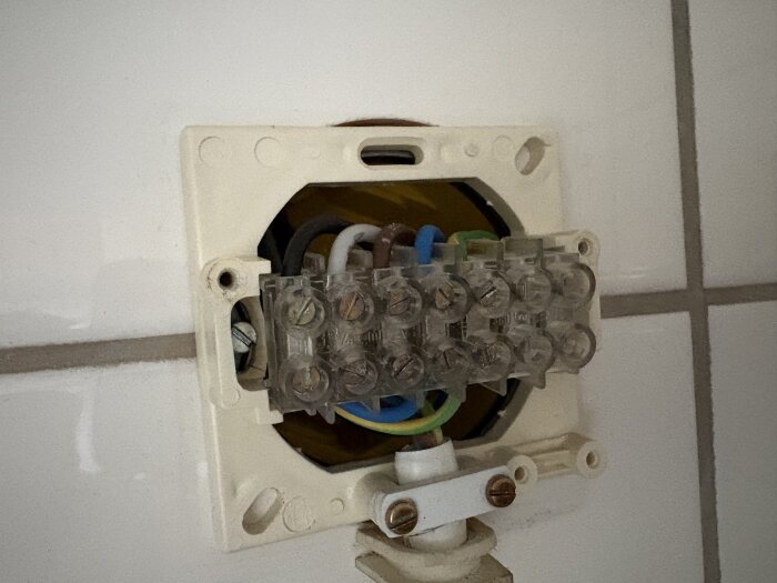 Anslutningspunkt för tvättmaskin med elektriska kablar och tre faser synliga under ett lock på en vägg.