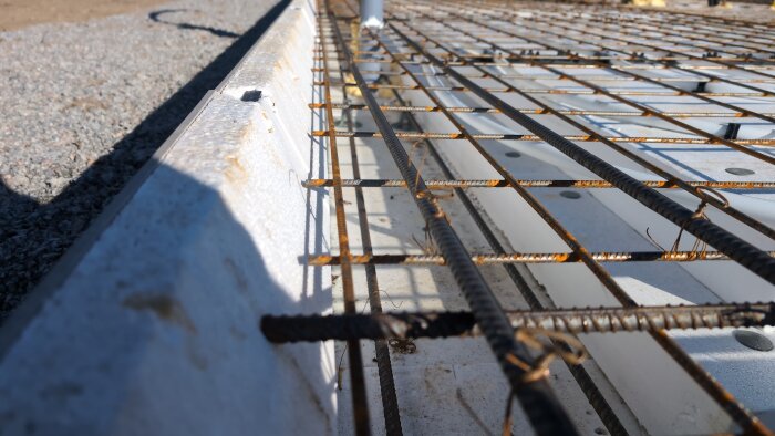 Bild av betongkant med armeringsjärn, något lutande, med grus i bakgrunden.