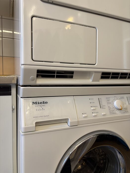 Torktumlare av märket Miele i närbild, del av ett staplat tvättmaskinssystem i badrum eller tvättrum.