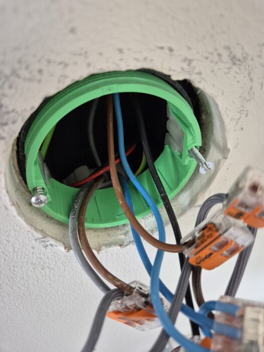 Grön elring med olika kablar och kopplingar synliga i en vägg, eldosan hänger delvis löst med skruvar på vardera sidan.