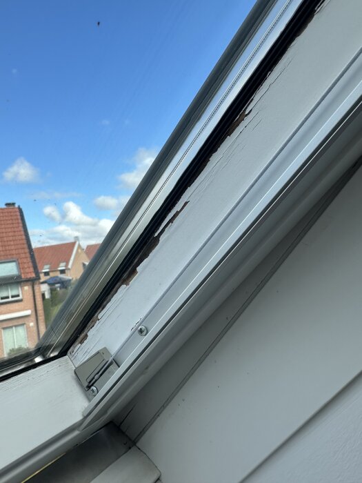 Fuktskadad träram på insidan av takfönster, synliga avflagnade färgflagor, klarblå himmel i bakgrunden, torr yta utan märke av murkenhet.