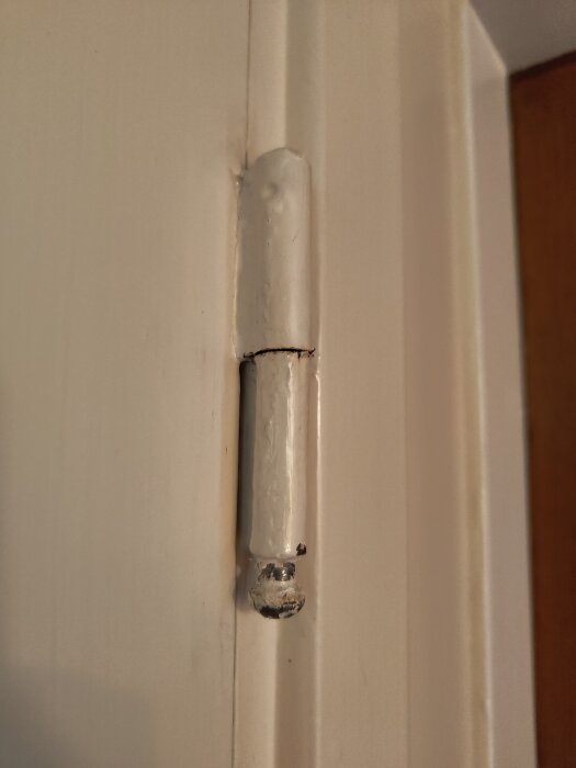 Närbild på ett gammalt vitmålat dörrgångjärn där dörrens dörrblad och karm syns, eventuellt från 1950-talet.