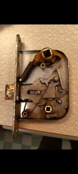 Närbild av en gammal metallisk låskista med inre mekanik synlig, inklusive fjäder och andra komponenter. Låset har mekanikstrul.