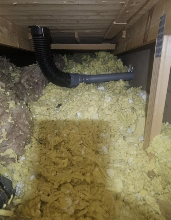 Gult isoleringsmaterial på vinden med en koppling av svarta och grå rör, tecken på otillräcklig avrinning och potentiell fuktspridning.