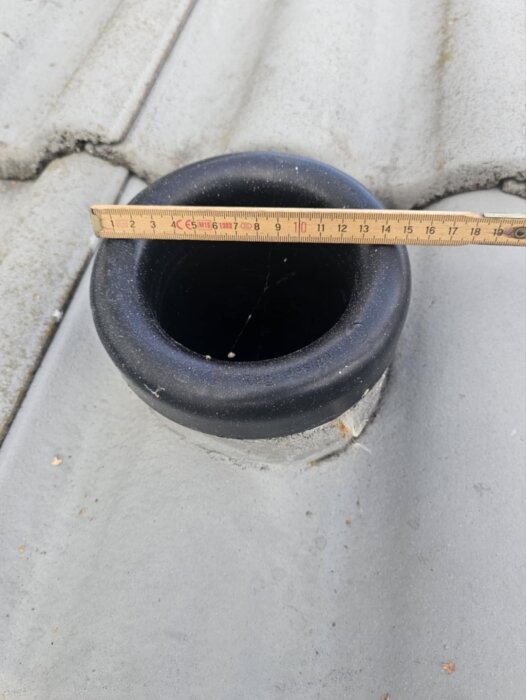 Avluftningsrör på tak utan regnskydd, med en linjal som mäter dess diameter.