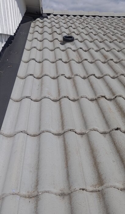 Grått tak med tegelpannor och en svart avluftare synlig. Inga regnskydd ses ovan avluftaren.助手