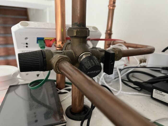 Kopparrör och ventiler ovanpå en värmepanna omgivna av diverse elektronik och kablar.