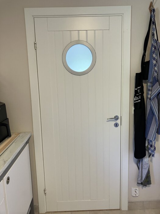 Omlackad vit dörr med runt fönster, klart dörrprojekt inomhus.