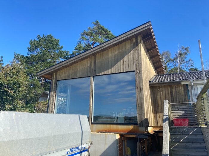 Uppdaterad fasad på ett hus med träpanel, där färgskiftningar och skuggor av överhäng syns tydligt mot en klarblå himmel.
