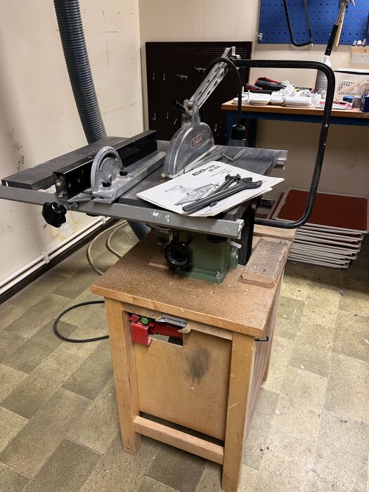 Inca Major bordsåg på arbetsbänk med manual och verktyg bredvid, utan skydd till drivrem. Finns i verkstadsmiljö.
