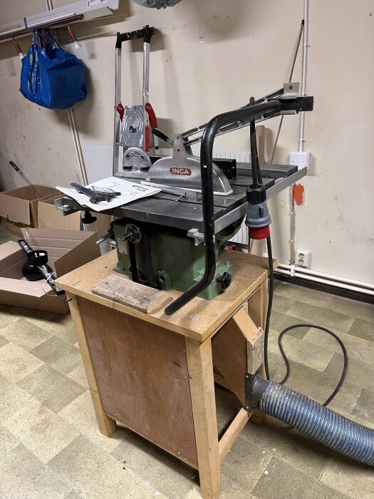 Inca Major bordsåg med avtagna sidobord och skydd; verktyg och manual syns, plasthink med slang ansluten för dammavlägsning.