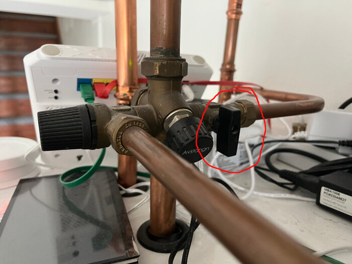 Ventil med svarta vred och kopparrör, en del är markerad med röd cirkel.
