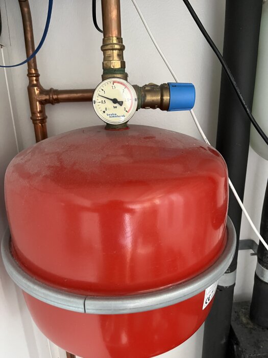 Röd expansionskärl och tryckmätare som visar 0,7 bar med röranslutningar i bakgrunden.