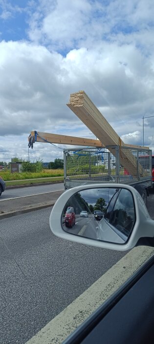 Lång last av träbalkar sticker ut från en släpvagn på motorväg.