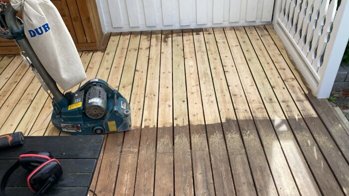 Golvslipmaskin används för att slipa träterrass, synlig skillnad mellan slipad och oslipad yta. Hörselskydd ligger på bordet.