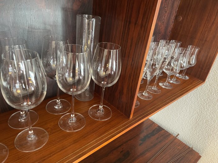 Vinglas och glasvaser på en hylla i ett vitrinskåp av trä.