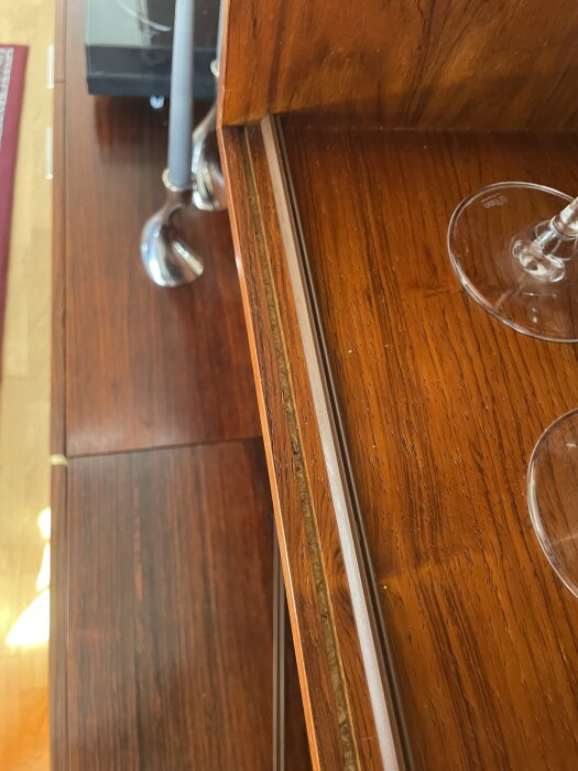 Äldre bokhylla med vitrinskåp där två spår syns för montering av glasskivor, samt en plastlist och del av ett vinglas på hyllan.