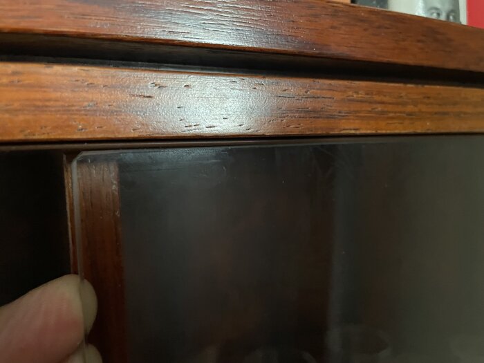 Glasruta som hålls med en hand i ett träramsspår, där spåret är nersänkt vilket gör att glaset riskerar att ramla ut när det flyttas mot mitten.