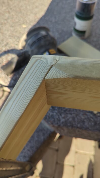 Närbild av hörnfog i ljust trä med synliga trämönster, placerad på ett bord utomhus med verktyg i bakgrunden.