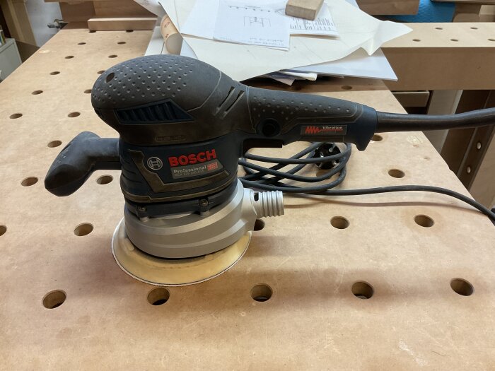 Bosch excenterslip GEX 125-150 AVE på en verkstadsbänk med träytor och hål för verktygsfäste i bakgrunden.