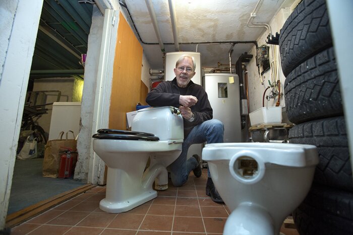 Man sitter i källare med gammal toalett och reservdelar, omgiven av sanitetsprodukter och däck.