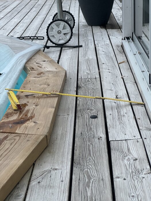 Trätrall med måttband bredvid en betongsockel nära vatten, med en vägg och hjul i bakgrunden.