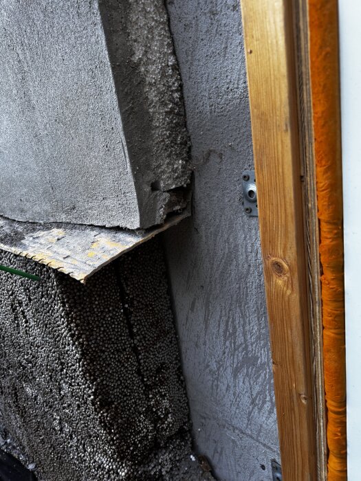 Närbild av husfasad med puts, synlig cellplastisolering och lecablock. En träregel syns till höger i bilden.