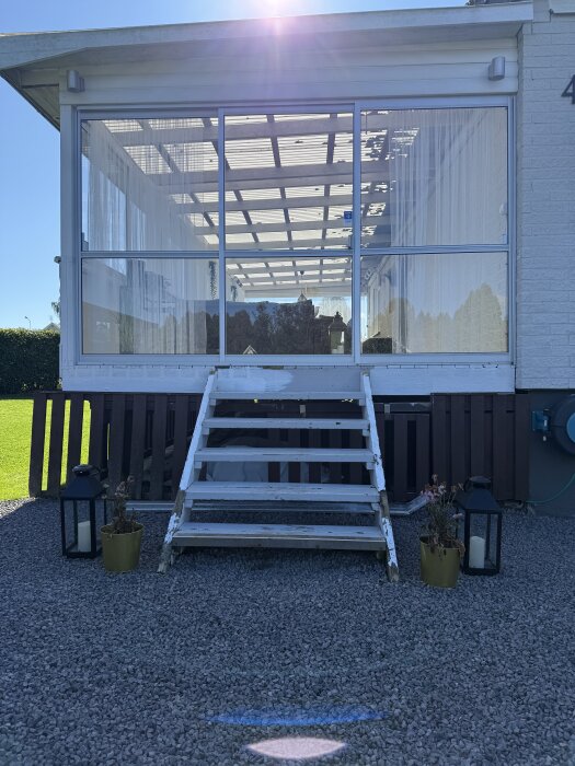 Vit entrétrappa framför en inglasad altan, omgiven av prydnadsväxter och lyktor, påbörjat projekt för att klä in altanen med liggande trall.