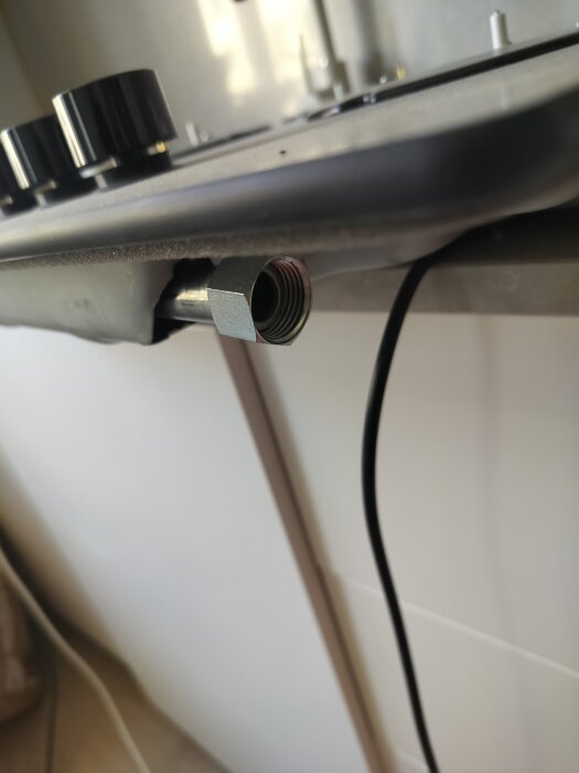 Gashällsundersida med metallkoppling synlig, baktill på enheten, mot en vit bakgrund i kök.