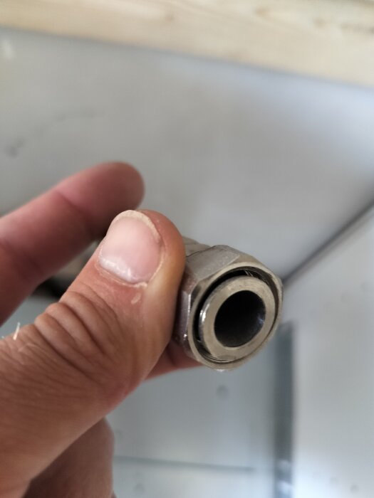 Närbild på en hand som håller en metallkoppling, eventuellt för anslutning till en gashäll i ett uteköksprojekt.