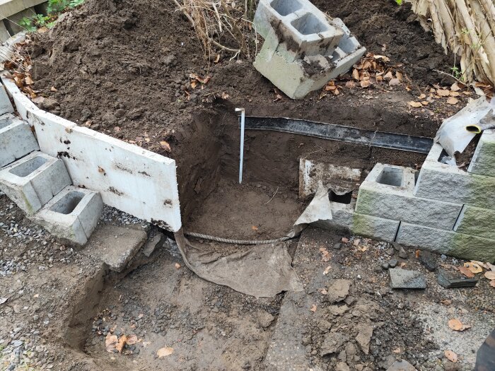 Delvis grävd mark med halvvägs byggd mur av betongblock och jordföreberedelser för ett byggprojekt i våras.