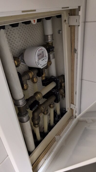 Bilden visar ett öppet skåp med röranslutningar och en vattenmätare, där en sötaktig lukt misstänks komma ifrån.