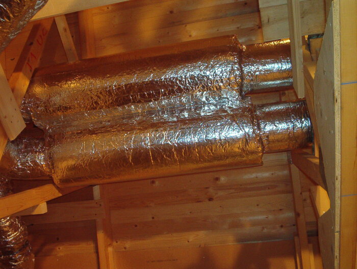 Kondensisolerade ventilationsrör i en kallvind, klädda med reflekterande lamellmatta för att motverka temperaturförluster.