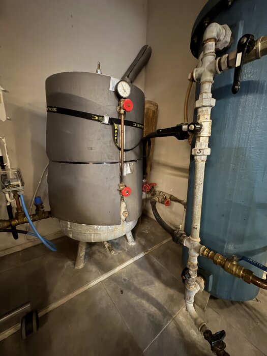 Förvaringstank med tryckmätare och rörledningar i ett förråd. Hydroforens manometer visar trycket. Problem med varierande vattentryck.