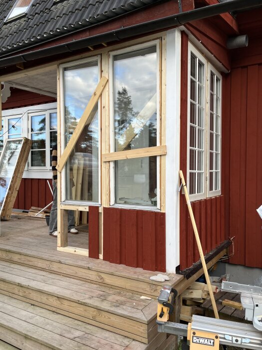 Röd husfasad under renovering med träbjälkar runt fönster, förberedelse för installation av en egentillverkad pardörr.