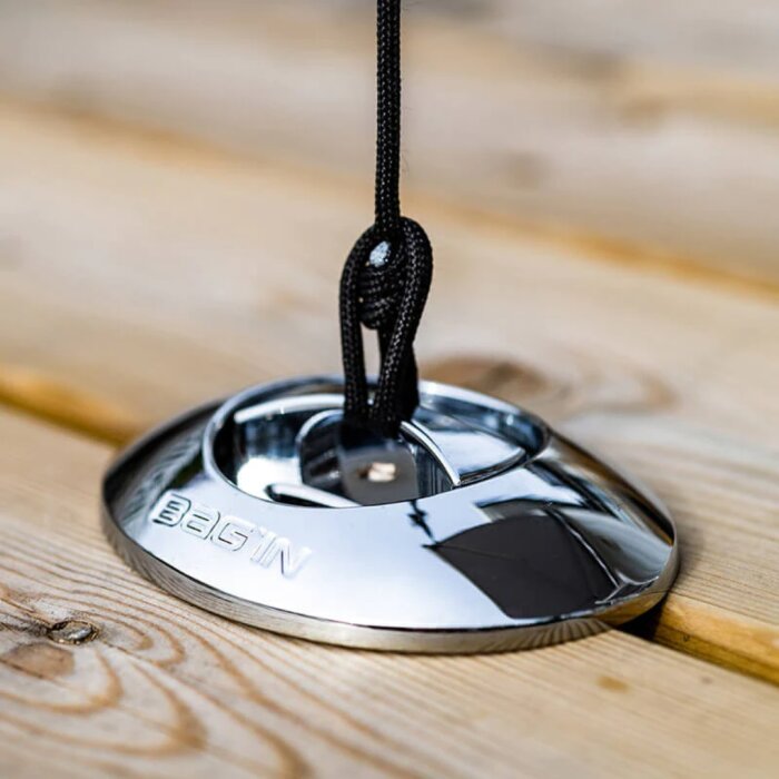 Stormankare av metall med svart rep för att förankra utemöbler, placerat på ett träbord.