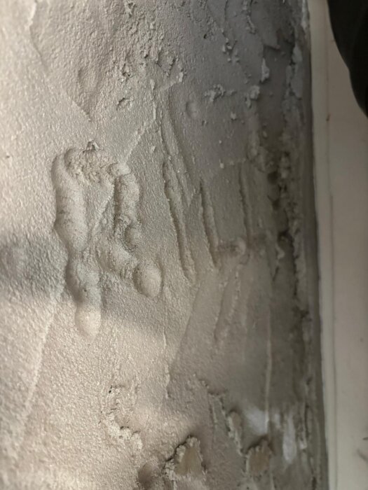 Närbild av nylagd puts på en vägg i en groventré, med ojämna ytor och spår av bearbetning.