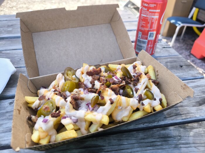 Smält ost och jalapeños på pommes i kartong med en Coca-Cola i bakgrunden på picknickbord.