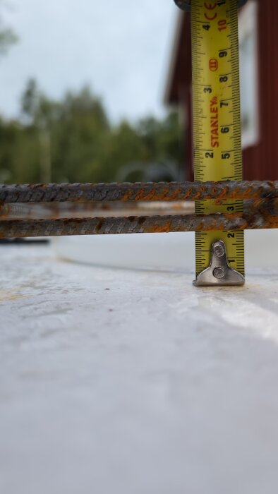 Mätband som visar höjd mellan rostiga armeringsjärn och underlag, cirka 30 mm, i utomhusmiljö.