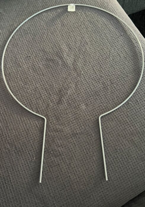 Metallväxtstöd i form av en cirkel med två ben placerad på en mörk textilyta.