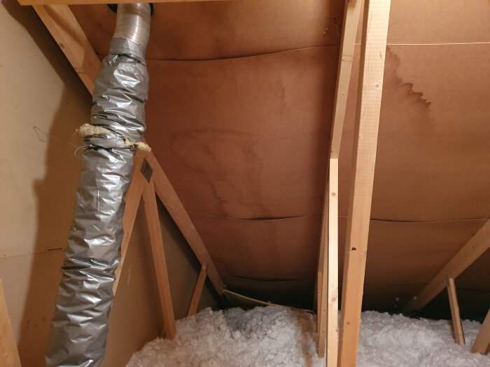 Isolerad imkanal i vind med silverfärgad isolerstrumpa och synlig trästomme; isoleringen lossnar och det finns oisolerade delar nära taket.