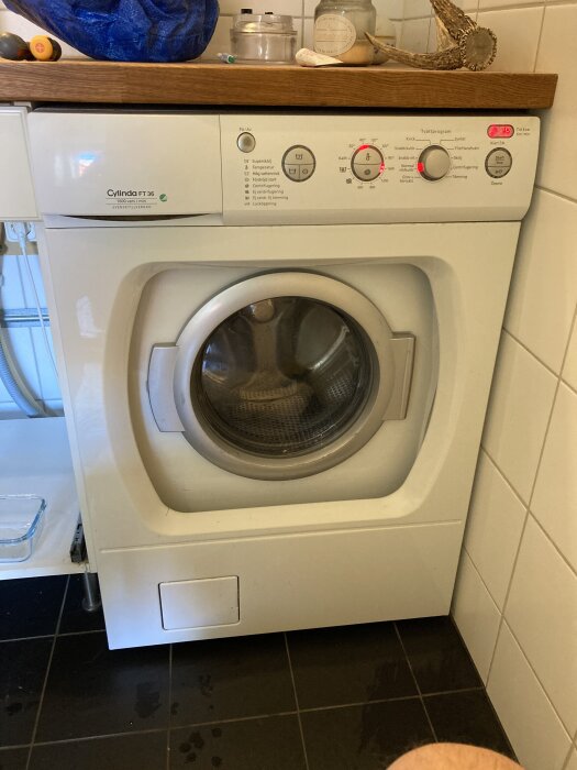 Cylinda FT 36 tvättmaskin i ett badrum, problem med att stanna och tömma vatten för tidigt. Finns olika programval på panelen.