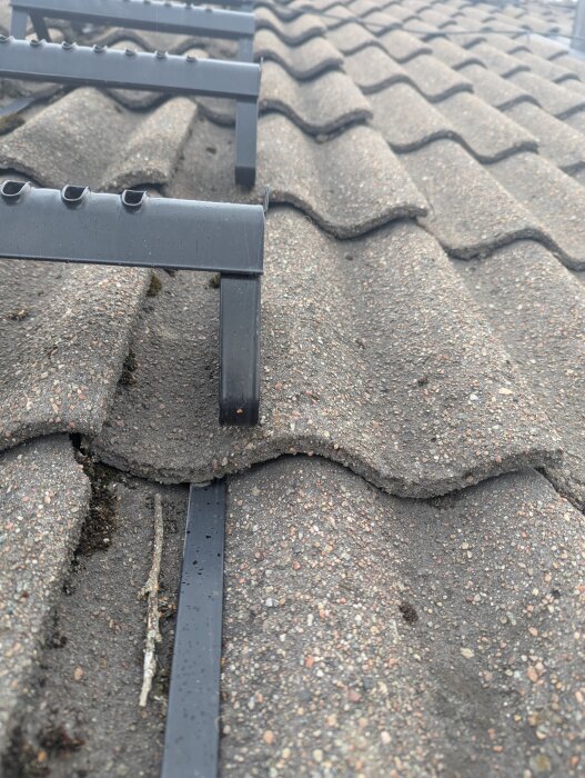 Takpannor med sprickor och monterade taksteg på ett tak, visar problem med takets skick och eventuell felaktig installation av stegen.