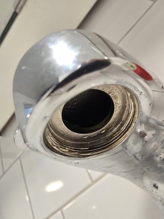 Närbild av en silverfärgad kran med ett avtaget munstycke, viss avlagring synlig.