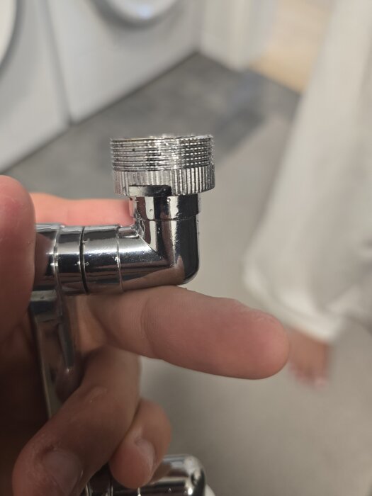 Man håller en kromad pipdel från en badrumsblandare med fokus på gängorna som verkar inte passa andra delar ordentligt.
