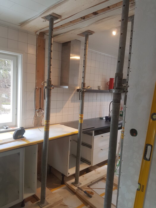 Byggnadsstöd används för att stödja bjälklag under en köksrenovering, med öppet tak och stöttande pelare i ett kök med vit kaklad vägg.