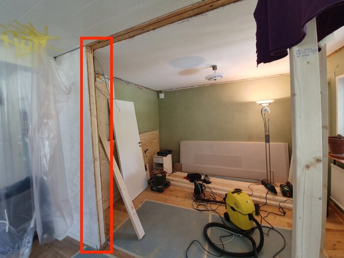 Bild på ett rum med en delvis riven vägg, uppstöttad med träreglar. Verktyg och byggmaterial syns på golvet.