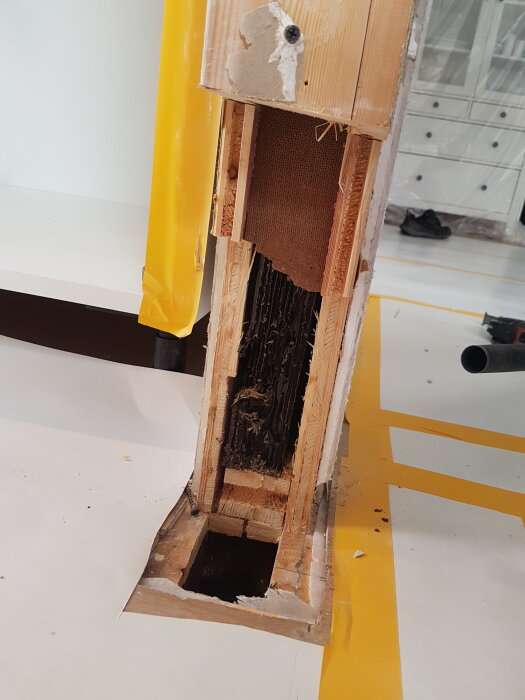 Öppet hål i golv med synlig konstruktion av en pelare i ett hus, inklusive träregel och isolering.