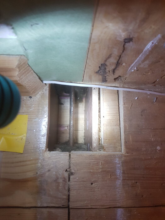 Hål i träbjälklag med synliga rör, belyst av en ficklampa.