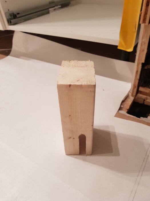 Träkloss med U-formad urtagning för att passa över en rundstång, placerad på ett vitt underlag framför hyllor.